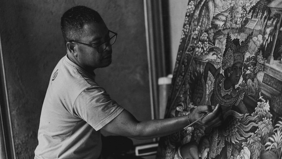 An artist skillfully paints a detailed Balinese canvas in monochrome.
