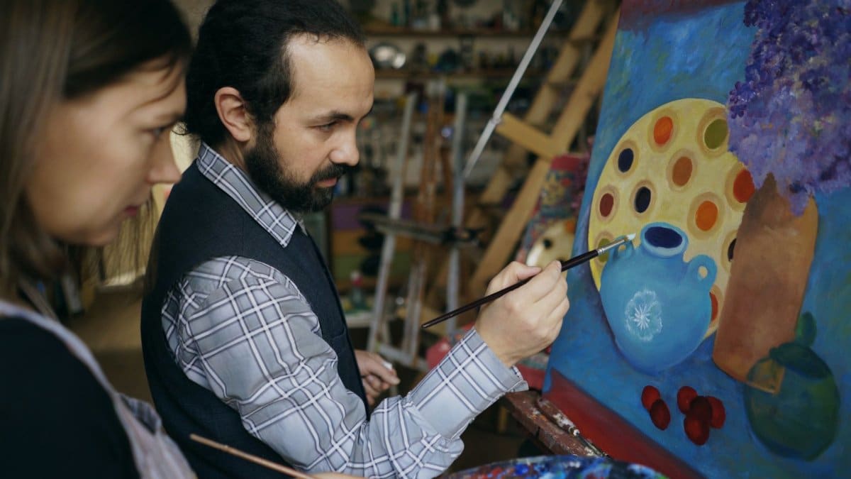 An art instructor teaches a student painting techniques in a studio setting.