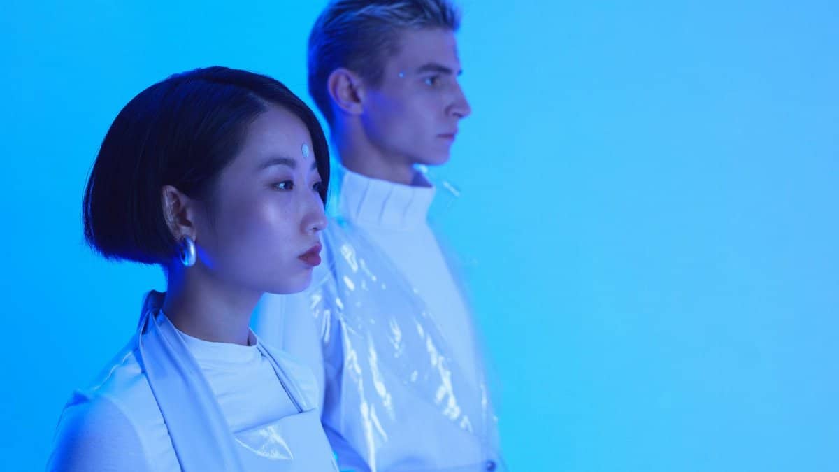 Futuristic fashion portrait of an Asian woman and Caucasian man in blue lighting, showcasing minimalist style.