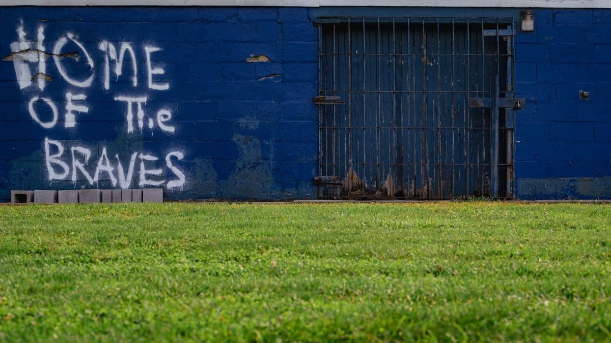 Graffiti reading 'Home of the Braves' on a blue brick wall with grass foreground.