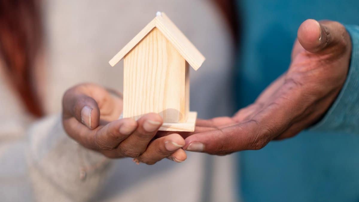 Close-up of hands holding a miniature wooden house, symbolizing home ownership and real estate investment.