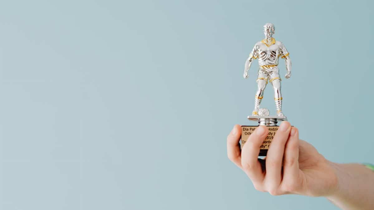 A hand holds a soccer trophy against a blue background, symbolizing success and achievement.