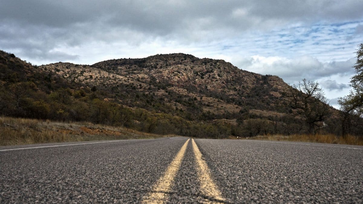 Empty road leading to the scenic Oklahoma mountains under a cloudy sky.