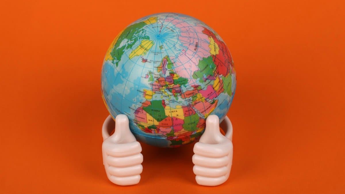 Vibrant globe model with thumbs-up figurines on orange background, symbolizing global positivity.