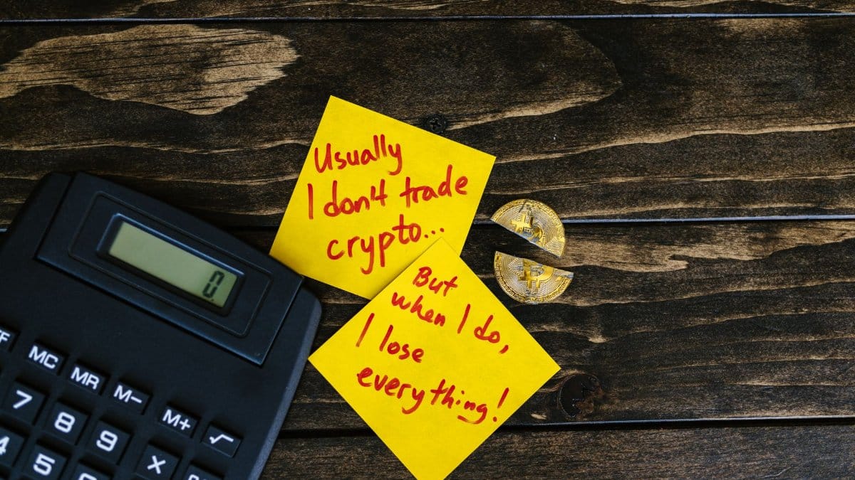 A satirical still life image depicting crypto investment risks with sticky notes, calculator, and broken coin.