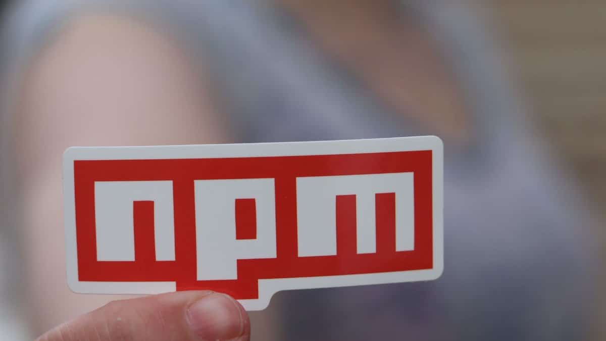 Blurred background close-up of a hand holding an npm sticker, ideal for web development themes.