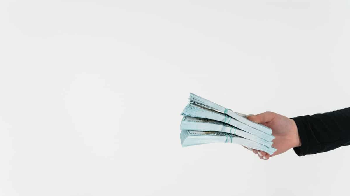 Close-up of a hand holding bundles of American dollar bills against a white background.