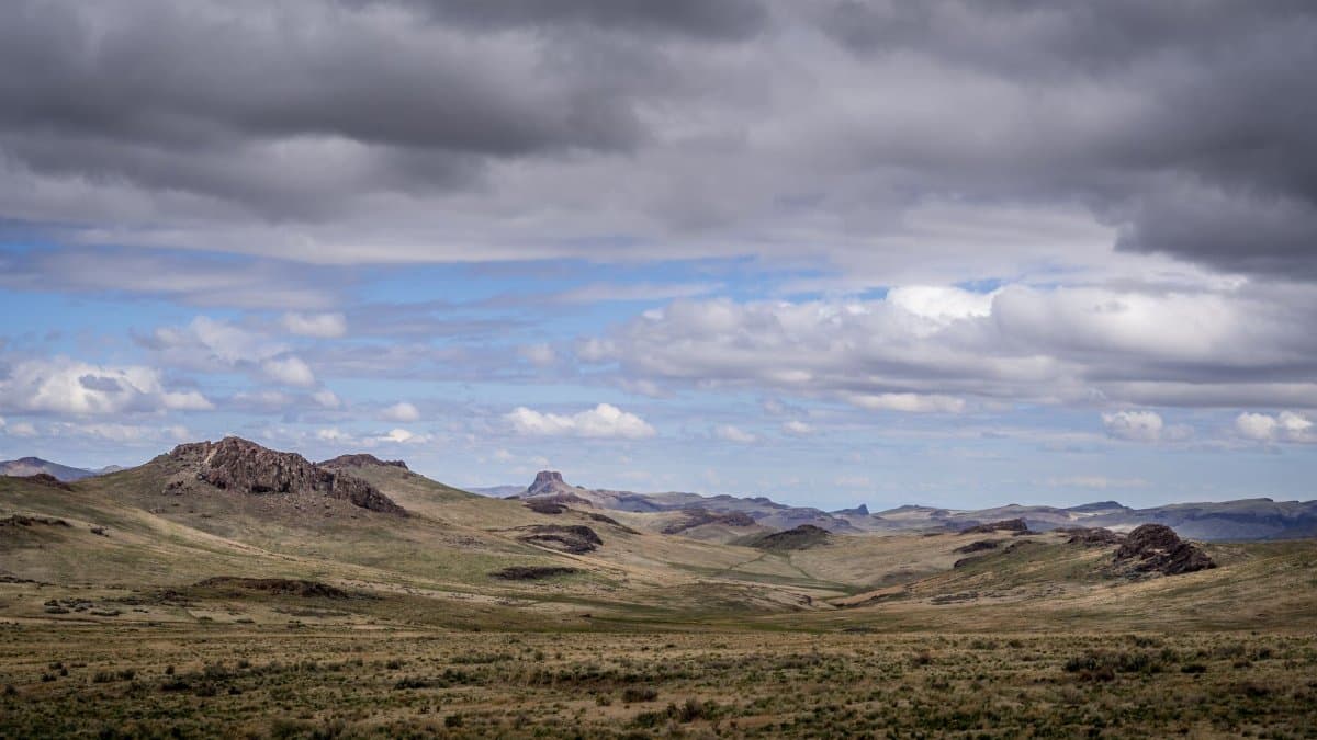 Spectacular landscape of field with dry grass and rocky hills in countryside under cloudy sky in daytime