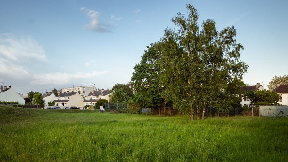 Suburban landscape with lush green field, trees, and houses under a clear sky in Compiègne, France.