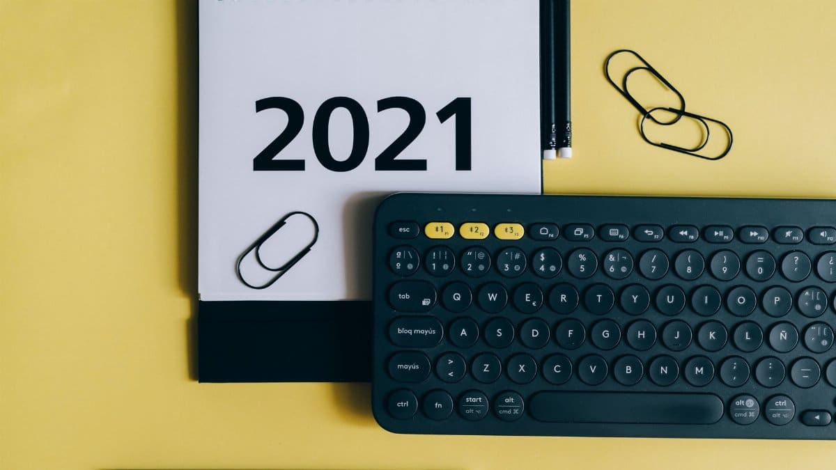 Flat lay of 2021 calendar, keyboard, and office supplies on a yellow background.
