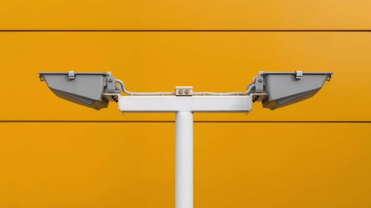 Minimalist street lamp with an industrial design set against a vibrant orange wall.