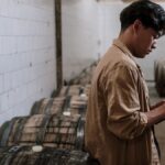 A craft beer expert inspects wooden barrels in a brewery's storage room.