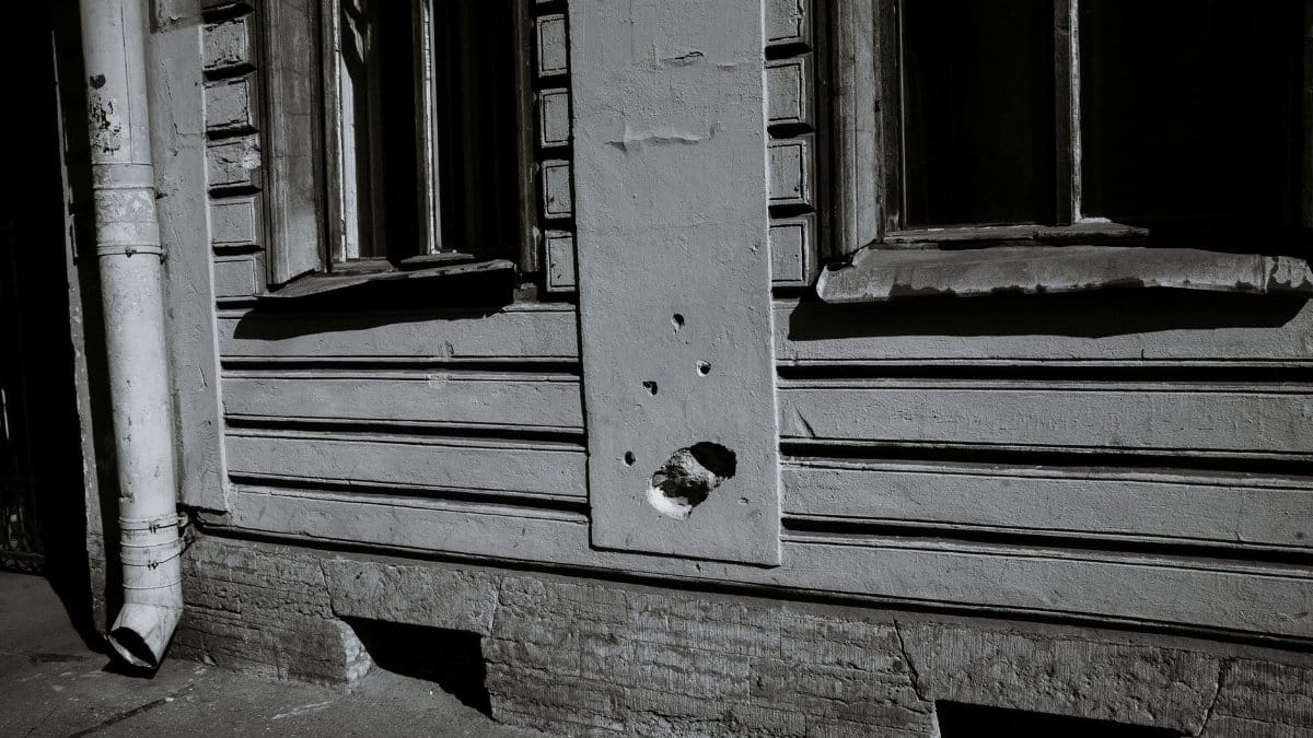 Abandoned urban building with broken windows and visible wall damage in black and white.