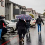 People walking on a wet street under a colorful umbrella during a rainy day.