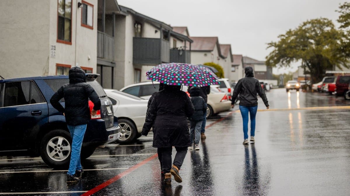 People walking on a wet street under a colorful umbrella during a rainy day.