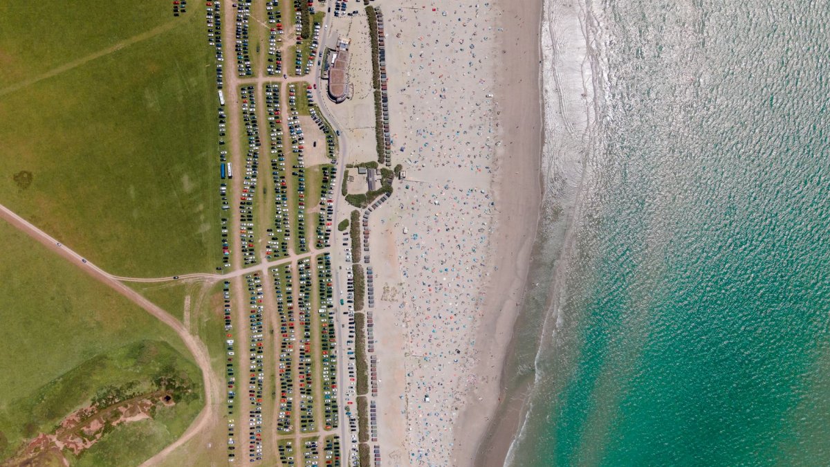 Discover the vibrant summer scene at West Wittering Beach from above, showcasing crowds and parked cars.