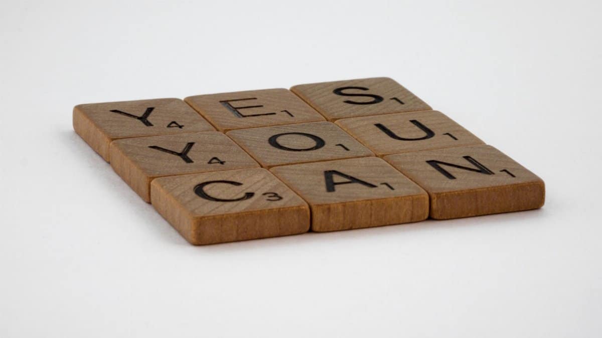 Wooden Scrabble tiles spelling 'Yes You Can' on a white background.