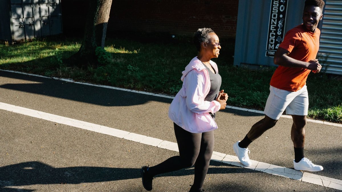 Two adults jogging outdoors on a sunny day, embracing a healthy lifestyle with smiles.