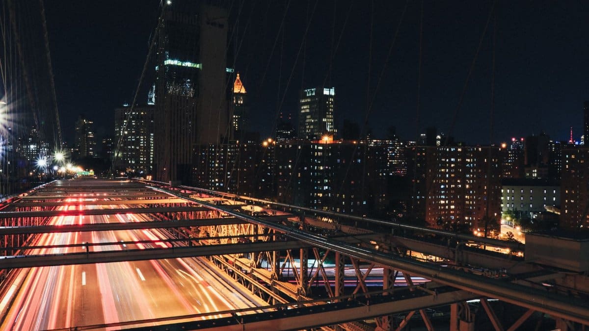 Long exposure shot capturing traffic on Brooklyn Bridge, NYC, at night with illuminated skyline.