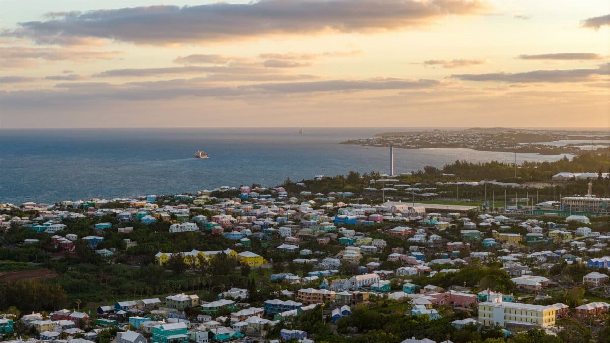 Stunning aerial view of Bermuda's coastal town with vibrant houses and ocean at sunset.