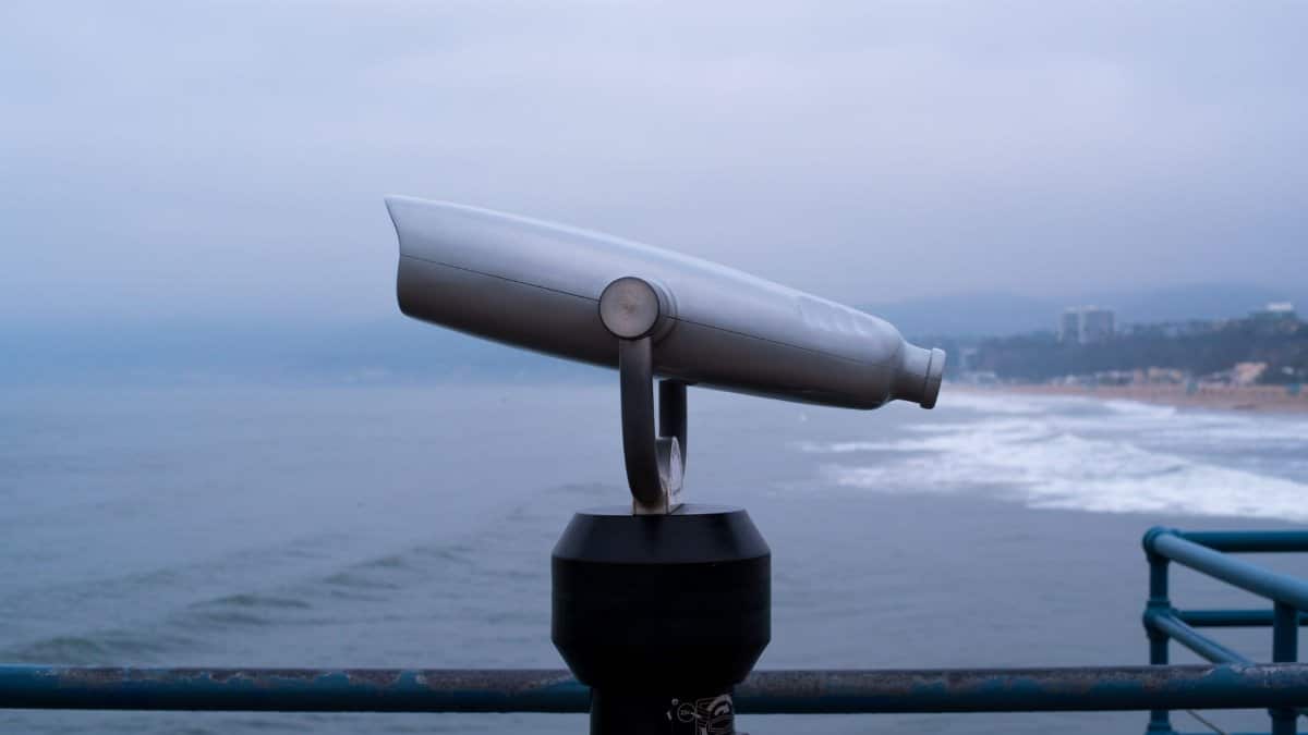 Public telescope overlooking the ocean from a seaside pier on a cloudy day.