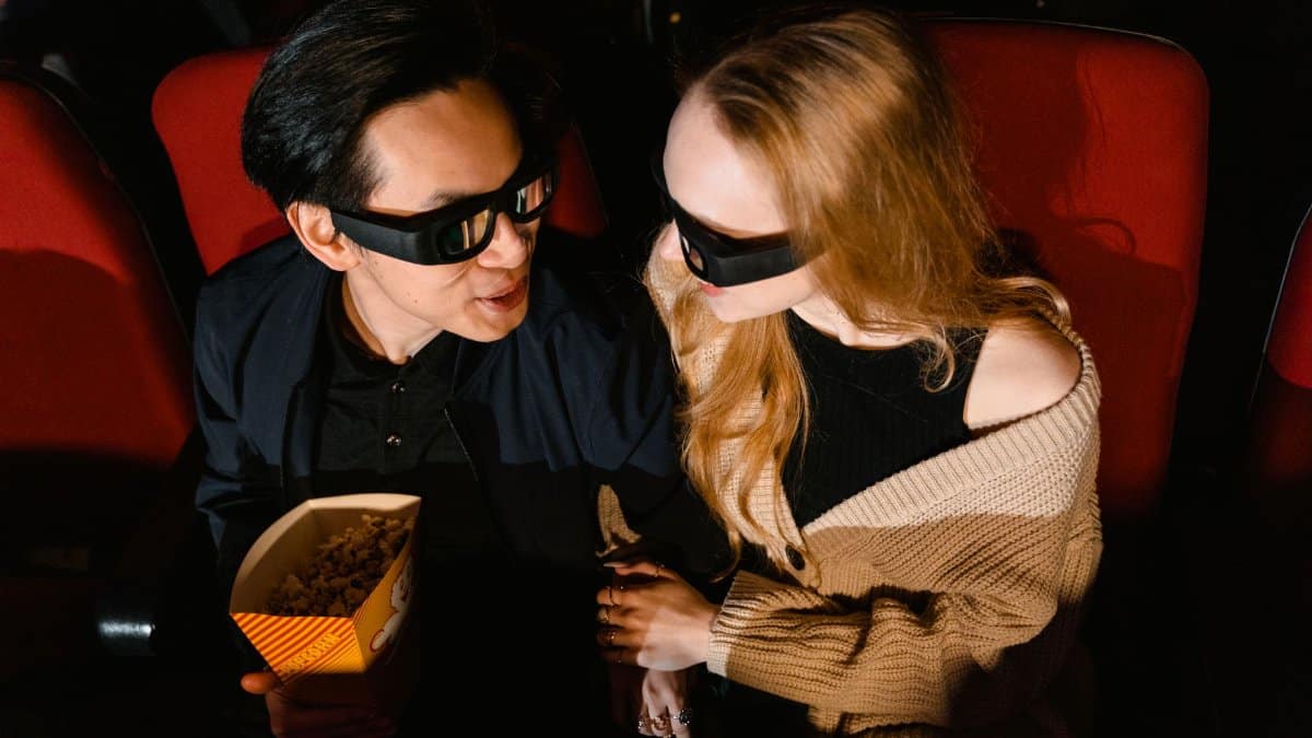 A couple wearing 3D glasses enjoying a movie with popcorn in a cinema.