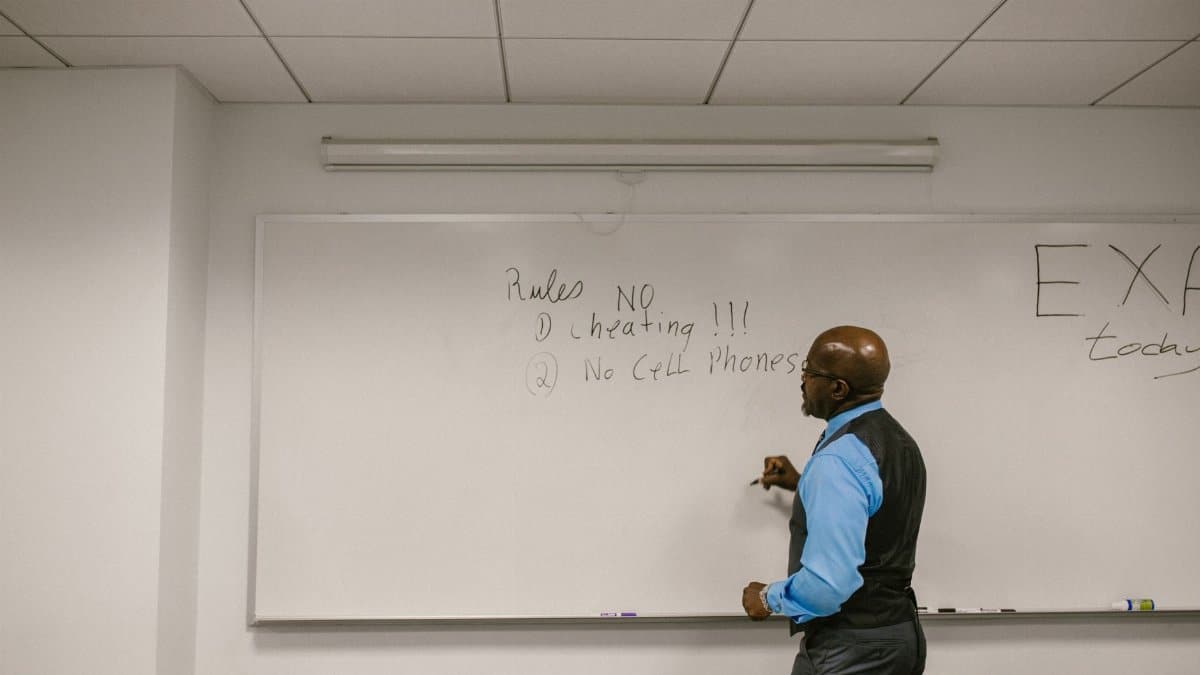 Instructor writing exam rules on a whiteboard in a college classroom.