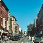 Vibrant street view of Hanover Street in Boston's North End with pedestrians and red brick buildings.