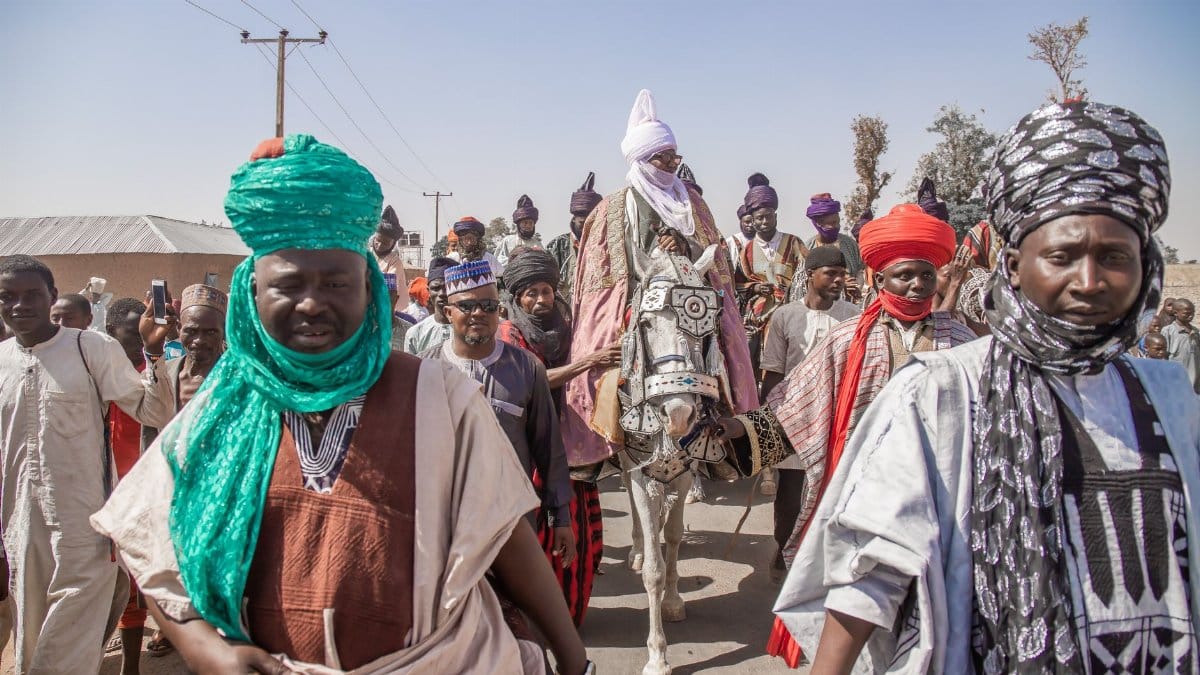 Vibrant celebration with men in traditional attire and turbans during a parade in Zaria, Nigeria.