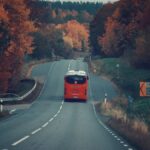A red bus travels on a picturesque highway through fall foliage in Jonkoping County, Sweden.
