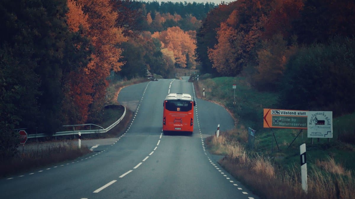 A red bus travels on a picturesque highway through fall foliage in Jonkoping County, Sweden.