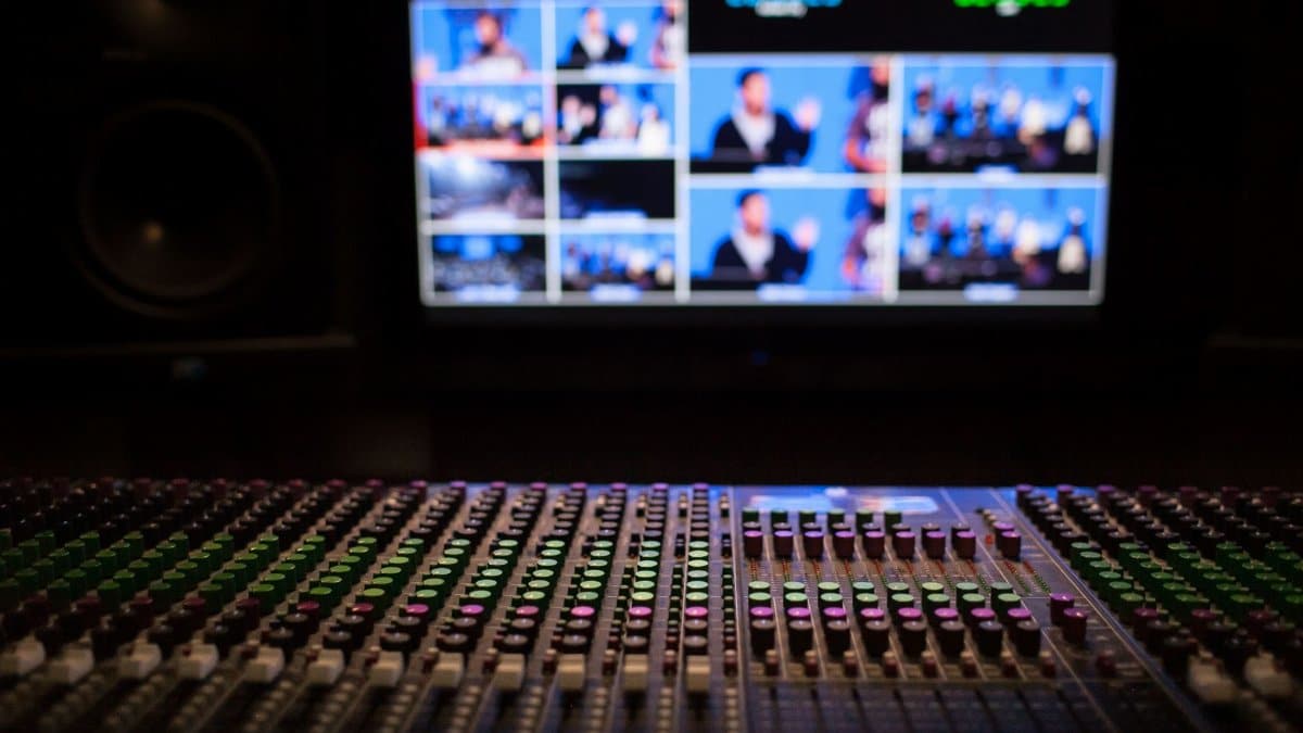 Close-up of a sound mixer with screens displaying video feeds in a professional studio setup.