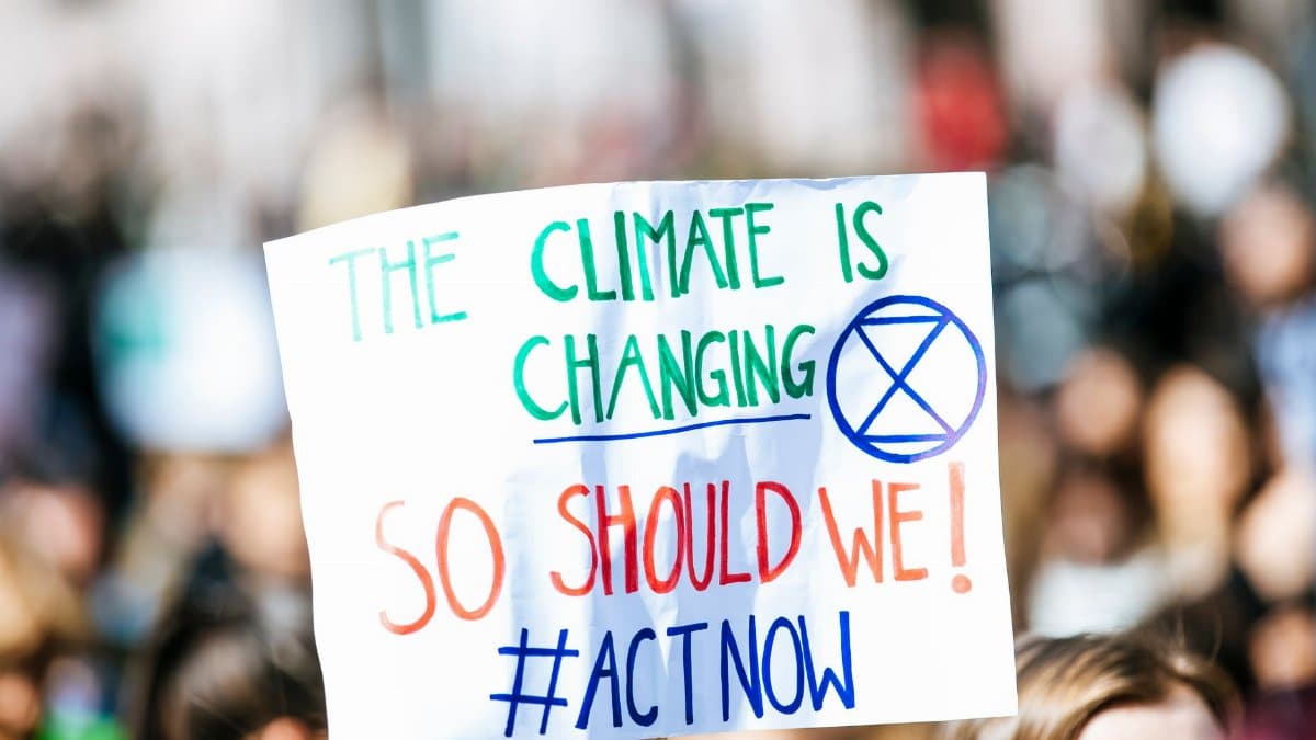 Crowd gathering for climate change protest, holding activist sign.