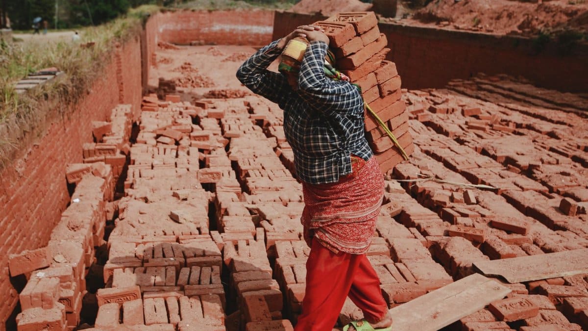 A woman carrying bricks at an outdoor construction site, showcasing labor and industry.