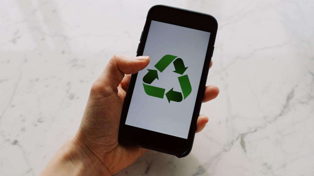 A close-up of a hand holding a smartphone with a recycling symbol on the screen, promoting sustainability and eco-consciousness.