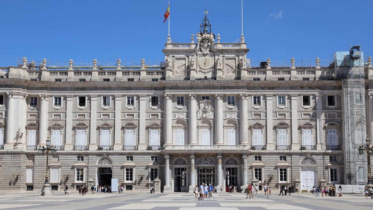 A clear day at the Royal Palace of Madrid with tourists in the plaza.