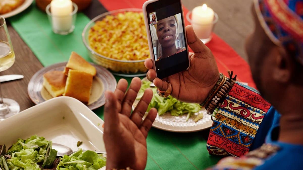 Man on video call celebrating Kwanzaa with vibrant feast.