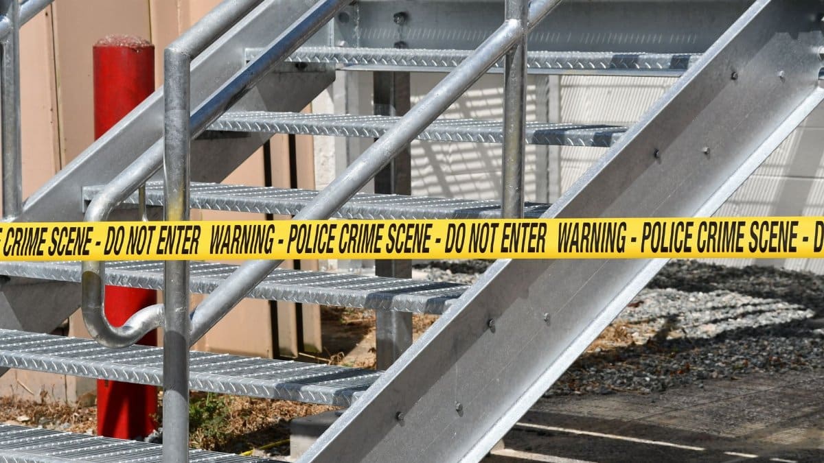 Close-up of a metal stairway blocked by yellow police crime scene tape outdoors.