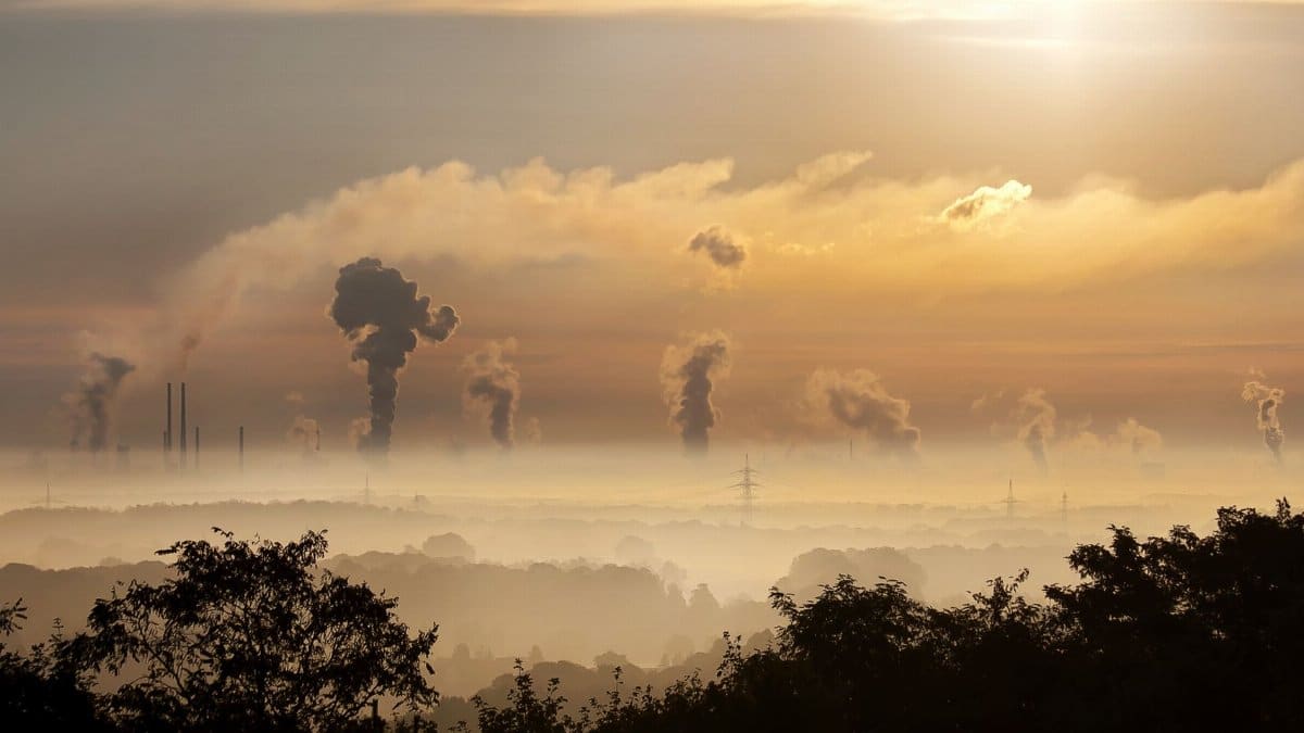 Smoke rising from factory chimneys at sunrise, symbolizing pollution and environmental impact.