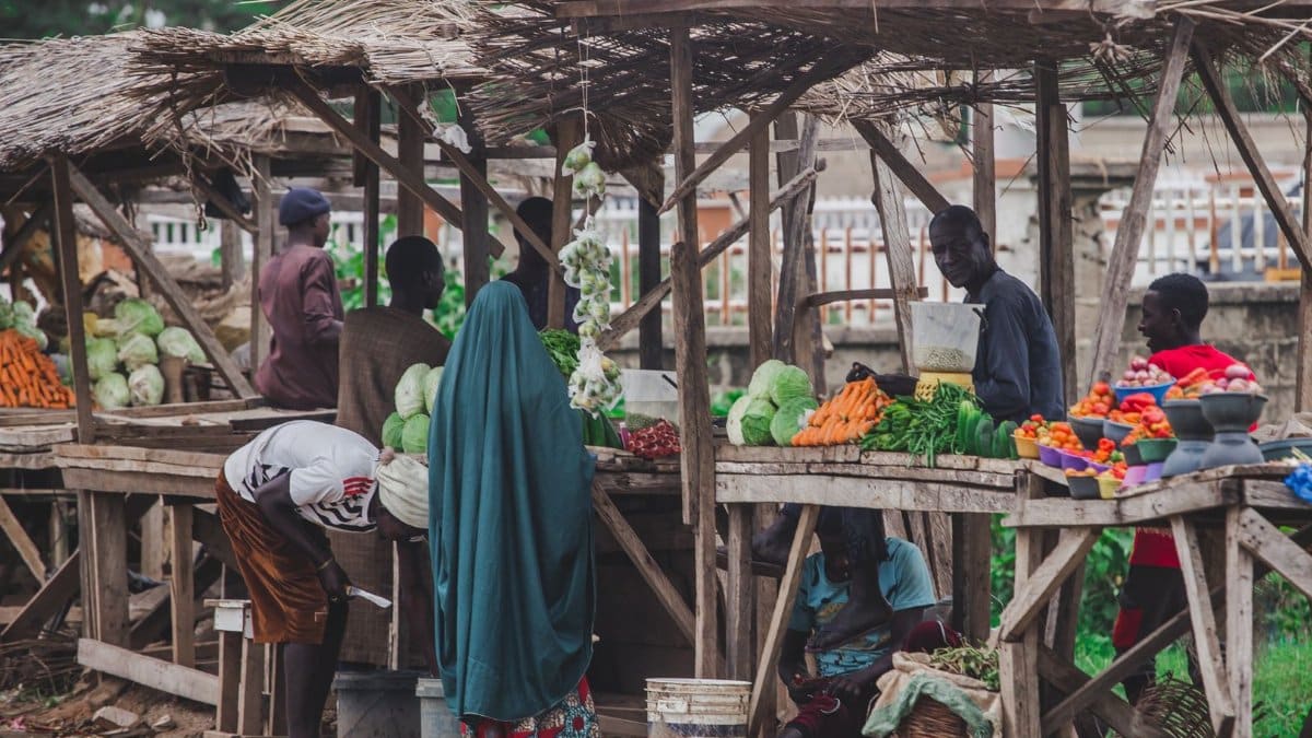 A bustling local market scene featuring fresh fruits and vegetables with diverse people interacting under rustic stalls.
