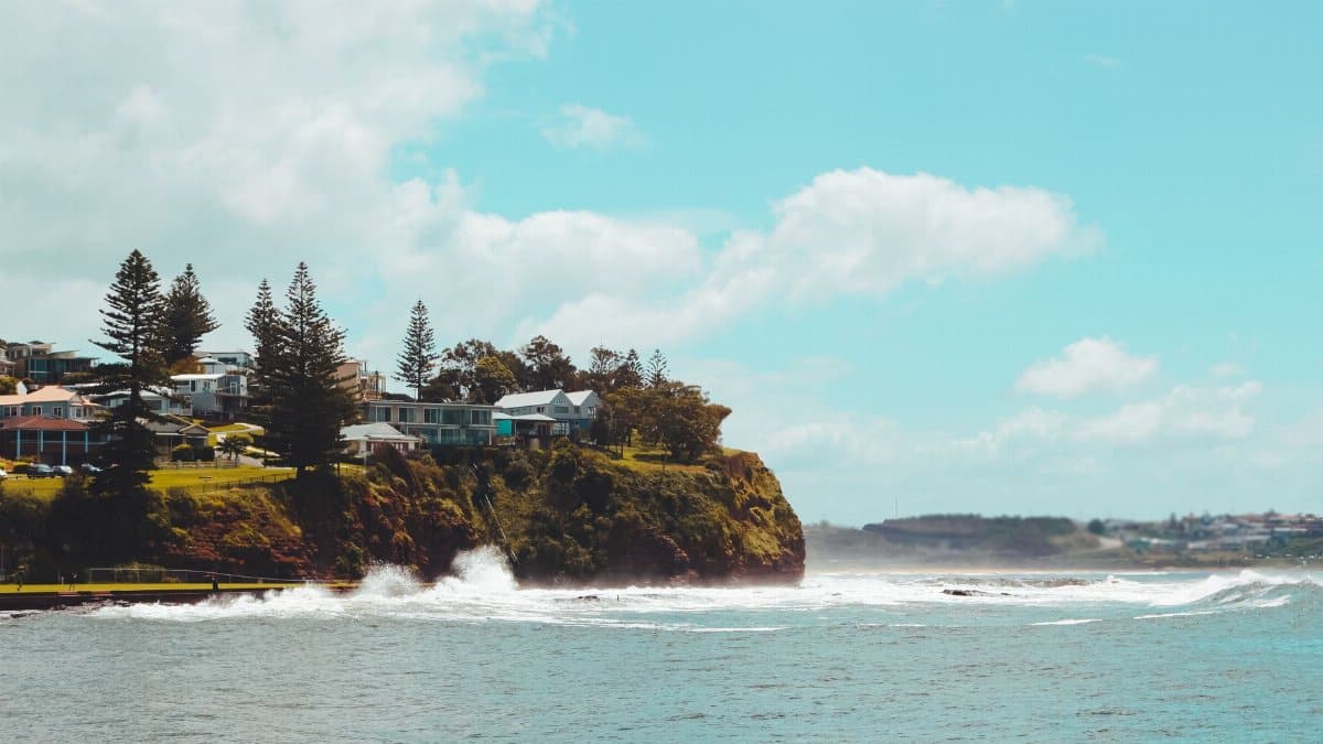 Beautiful coastal village in Australia with cliffs and ocean waves under a bright sky.