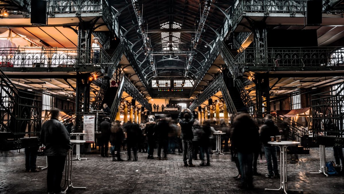 Busy indoor market with vintage iron architecture and bustling crowd, capturing urban commerce.