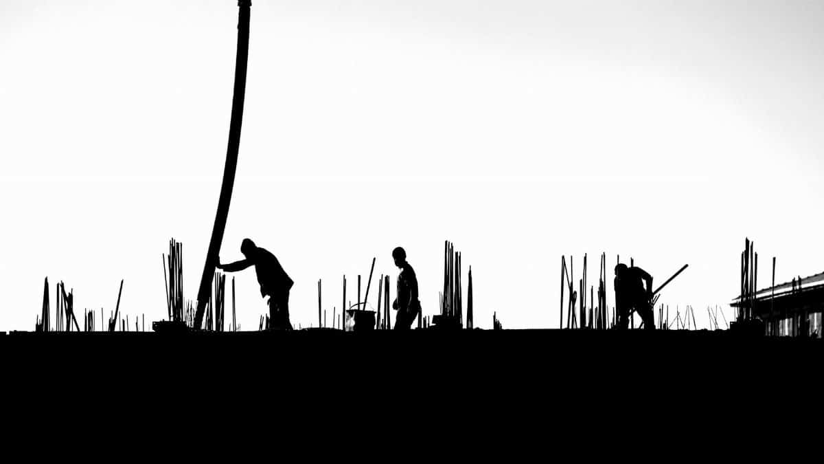 Black and white photo of construction workers silhouetted against the sky.