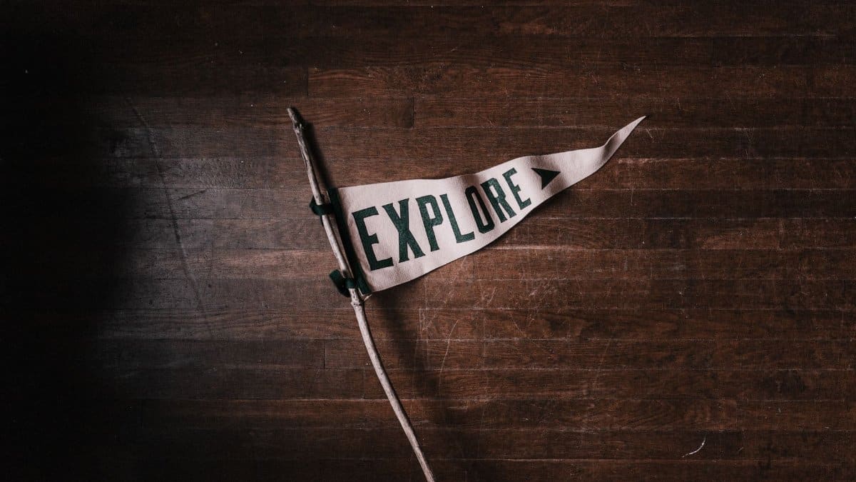 Artistic flat lay of an 'Explore' pennant on rustic wooden flooring, emphasizing adventure and exploration.