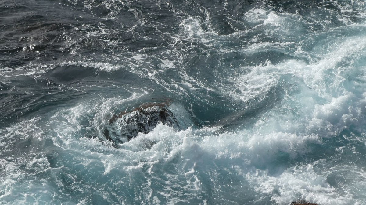 Aerial view of turbulent ocean waves crashing against rugged coastal rocks.