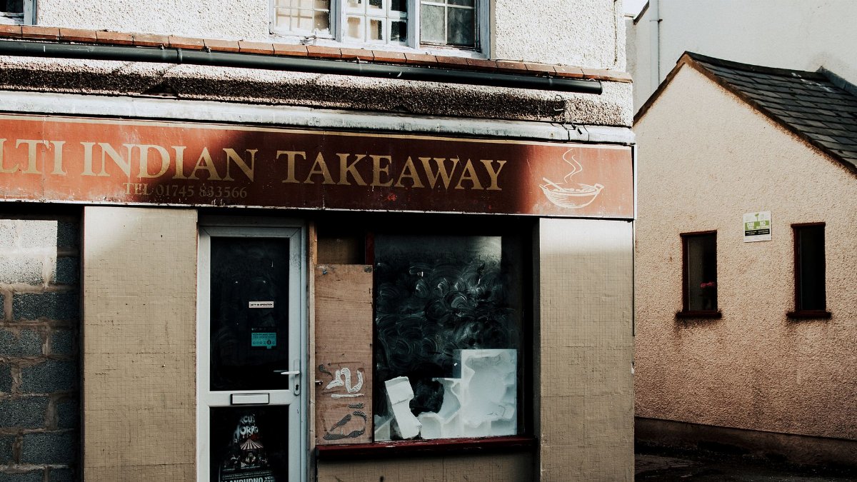 Exterior shot of an abandoned Indian takeaway restaurant with visible signage and boarded windows.