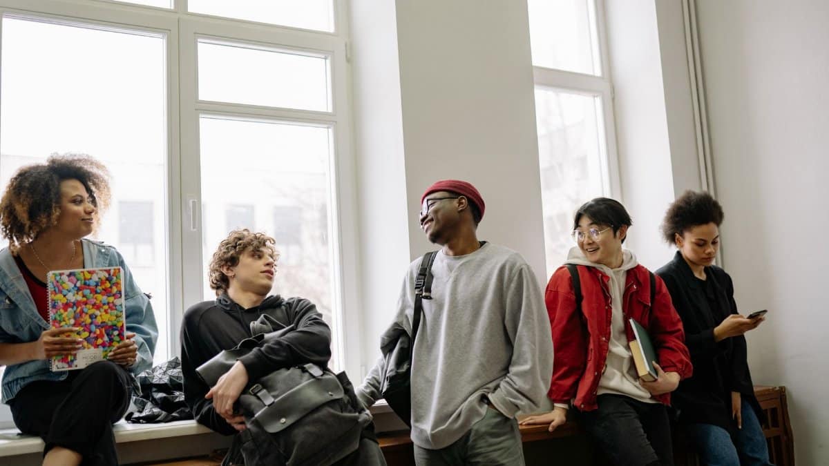 A diverse group of young adults socializing near a window sill, enjoying casual conversation.