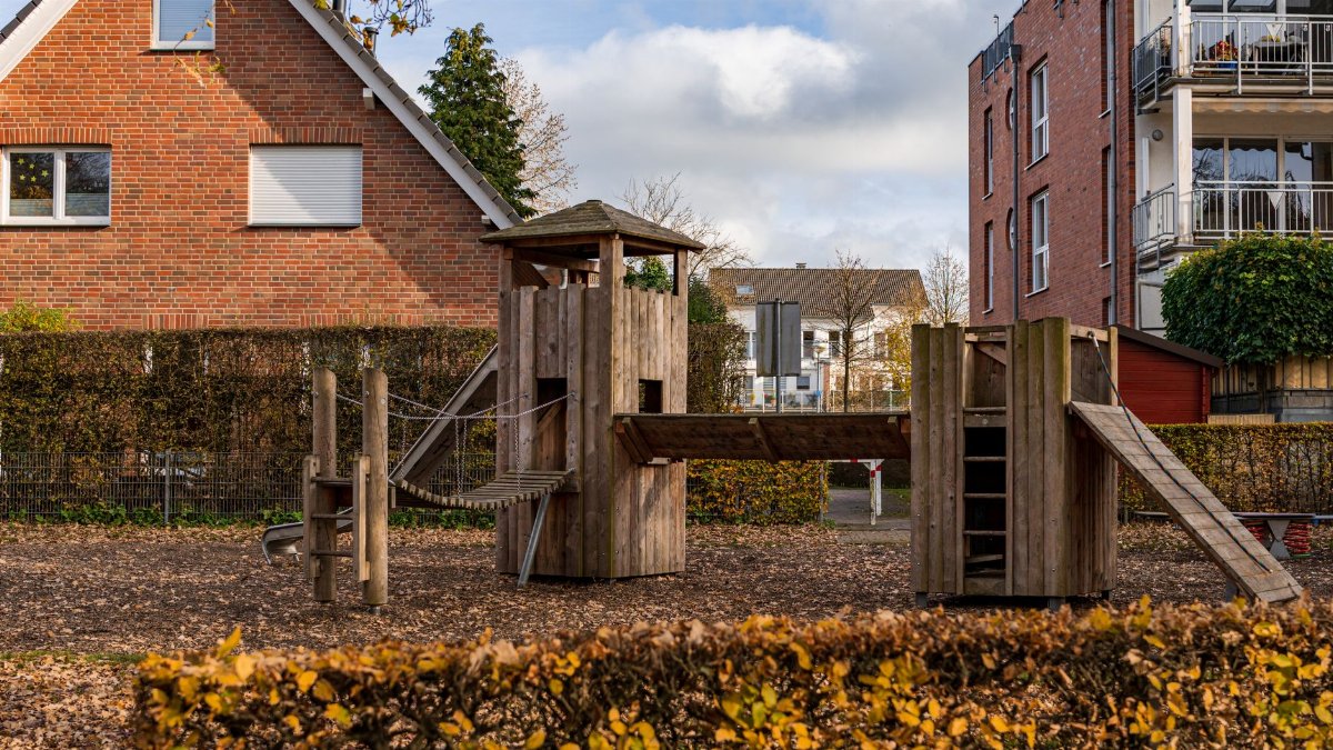 A cozy suburban playground featuring a wooden play structure surrounded by autumn foliage and residential buildings.