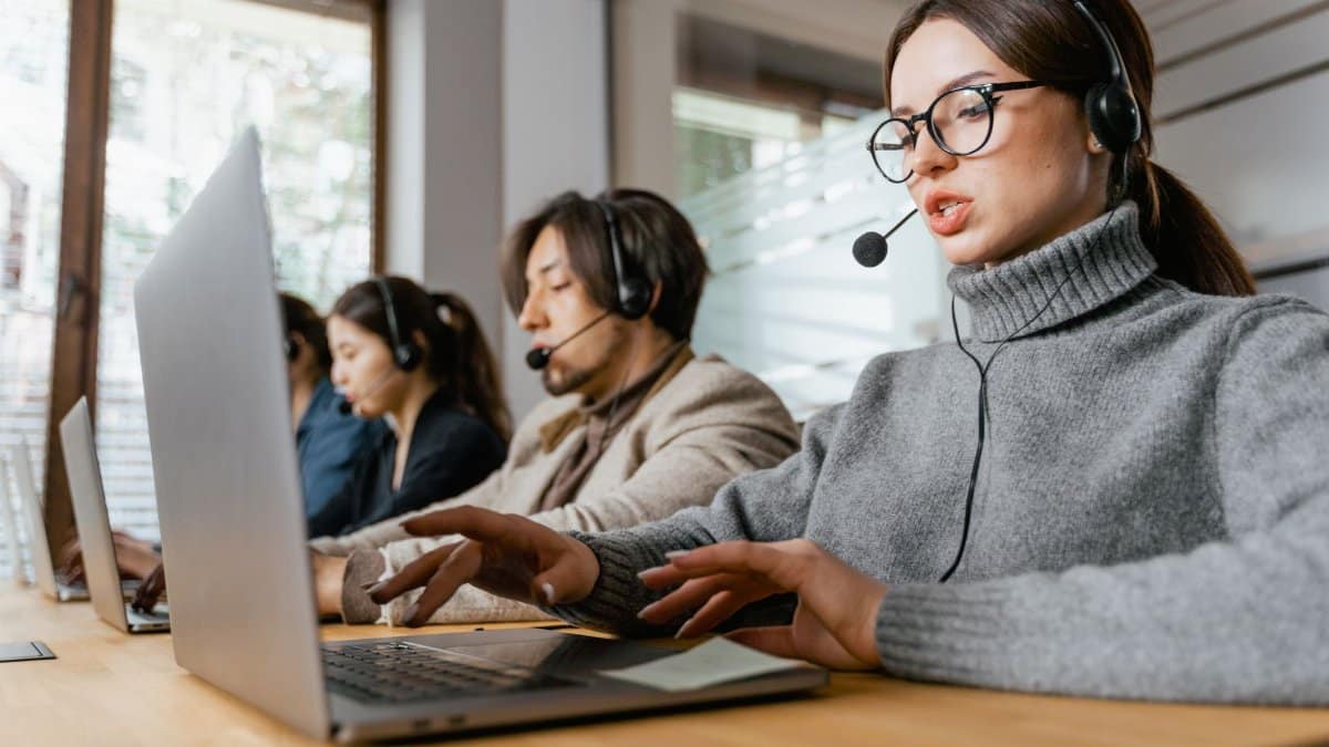 Four call center employees working with headsets and laptops in a modern office setting.