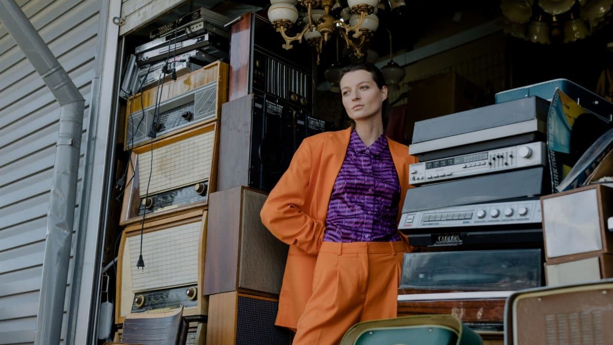 Woman in vibrant outfit posing with vintage audio equipment at an outdoor flea market.
